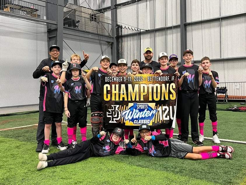 Youth baseball team celebrating a Winter Classic championship in custom black and pink Capra uniforms