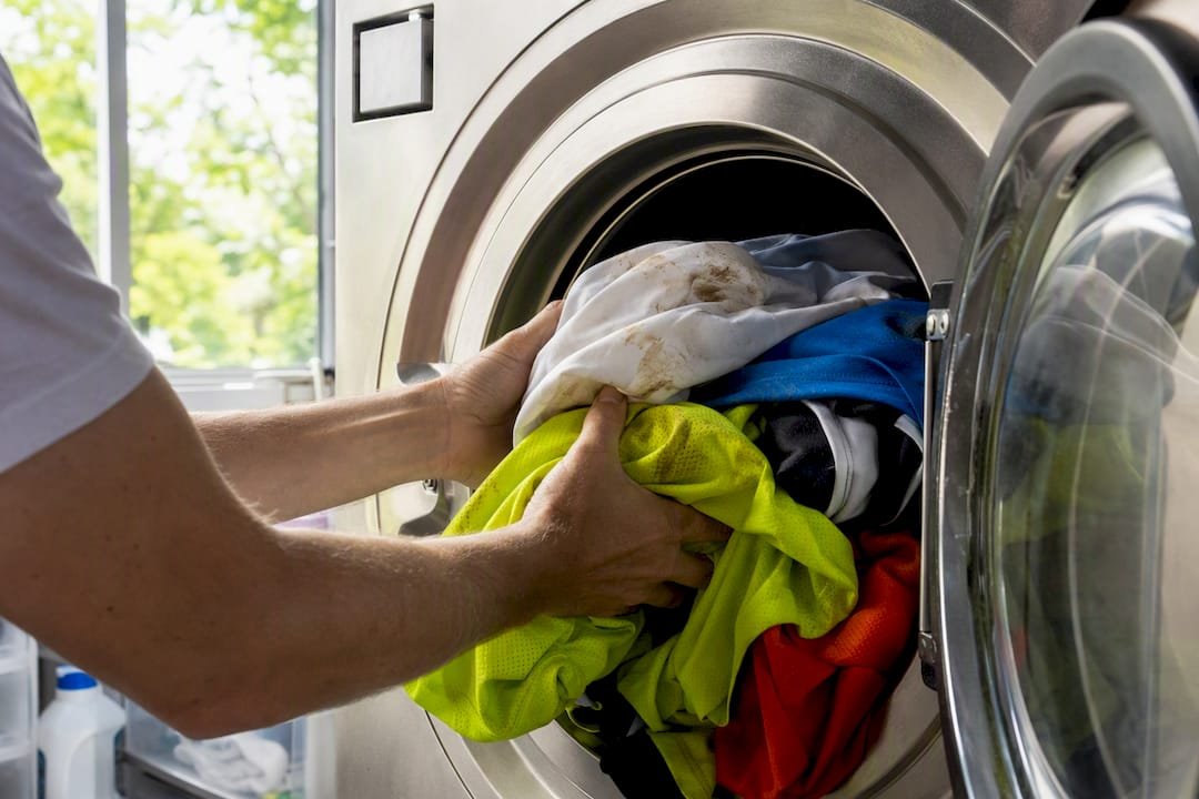 Hands loading sports uniforms into washing machine