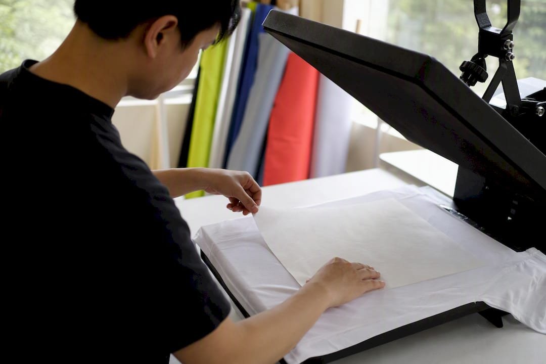 Hands aligning sublimation paper on fabric under heat press